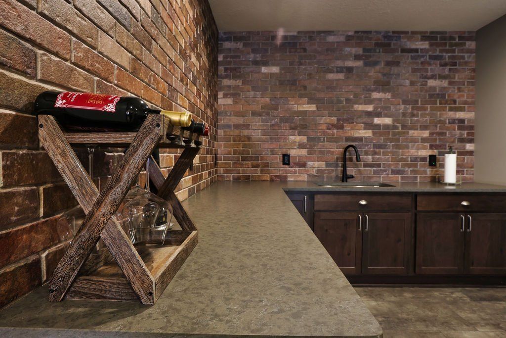Brick-walled bar with wine rack, counter, sink, and dark wood cabinets.