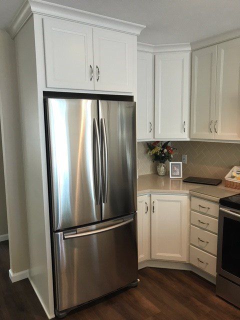 Stainless steel refrigerator built into white kitchen cabinets.