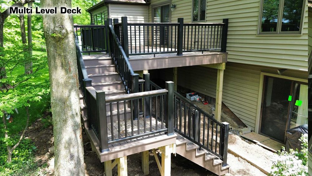 Exterior shot of a wooden deck and staircase with black railing, attached to a light-colored house surrounded by trees.
