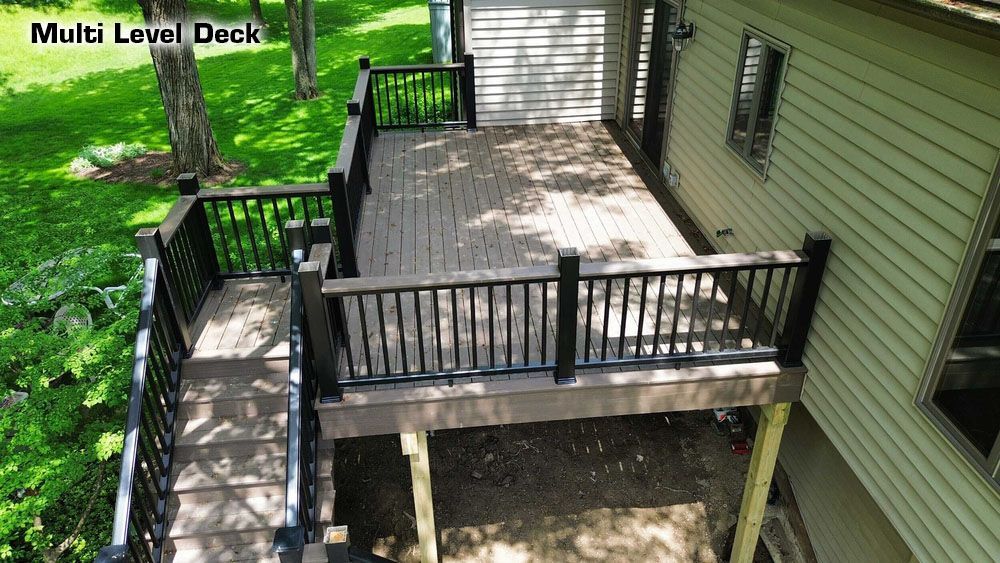 Elevated wooden deck with black railings, attached to a beige house, set in a grassy yard with trees.