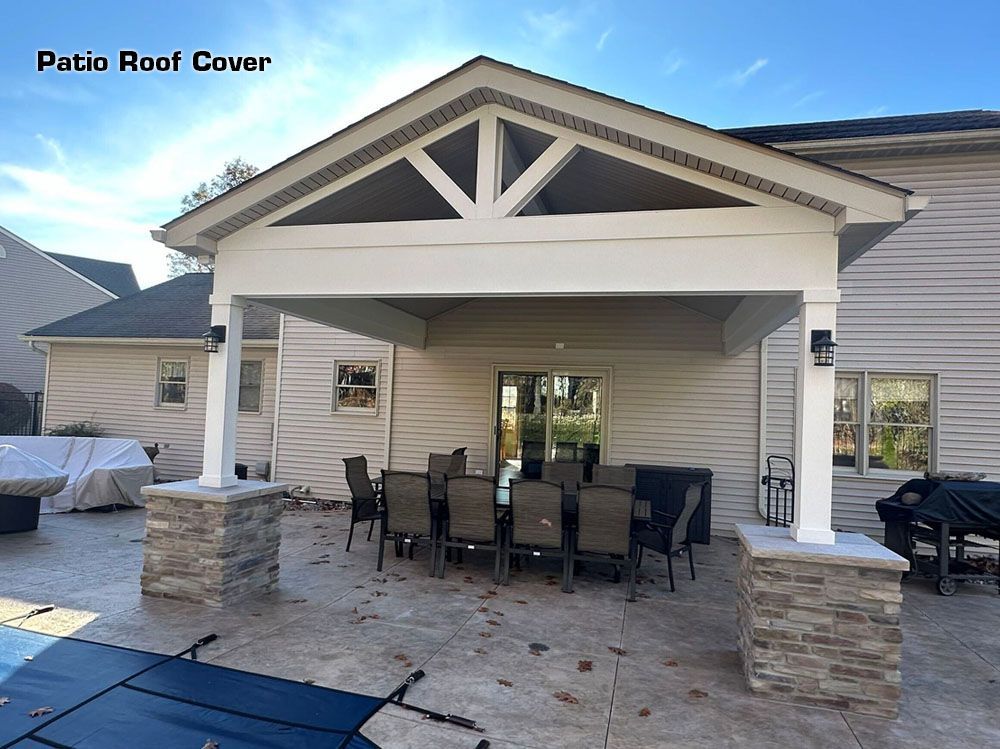 Covered patio with dining table and chairs outside a house. Stone columns and brown siding.