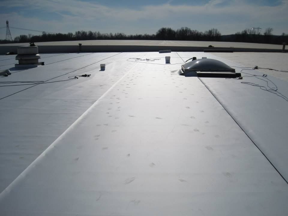 Flat, light-colored commercial roof with skylight, vents, and safety lines under a bright blue sky.