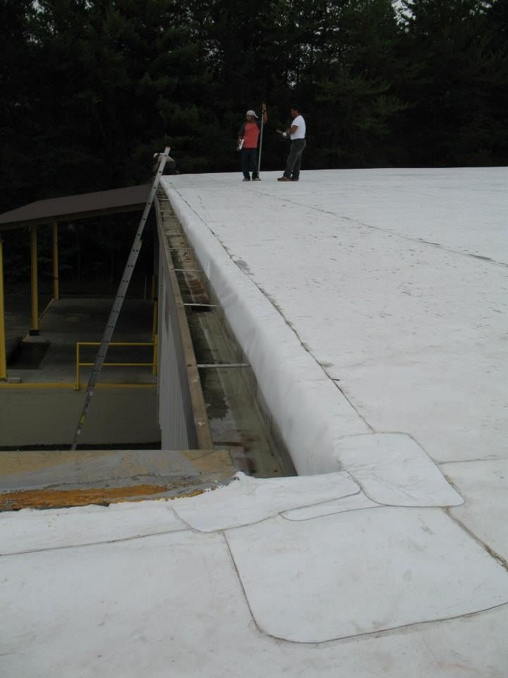 Two people on a white flat roof near a building with yellow supports; a ladder leans against the roof.