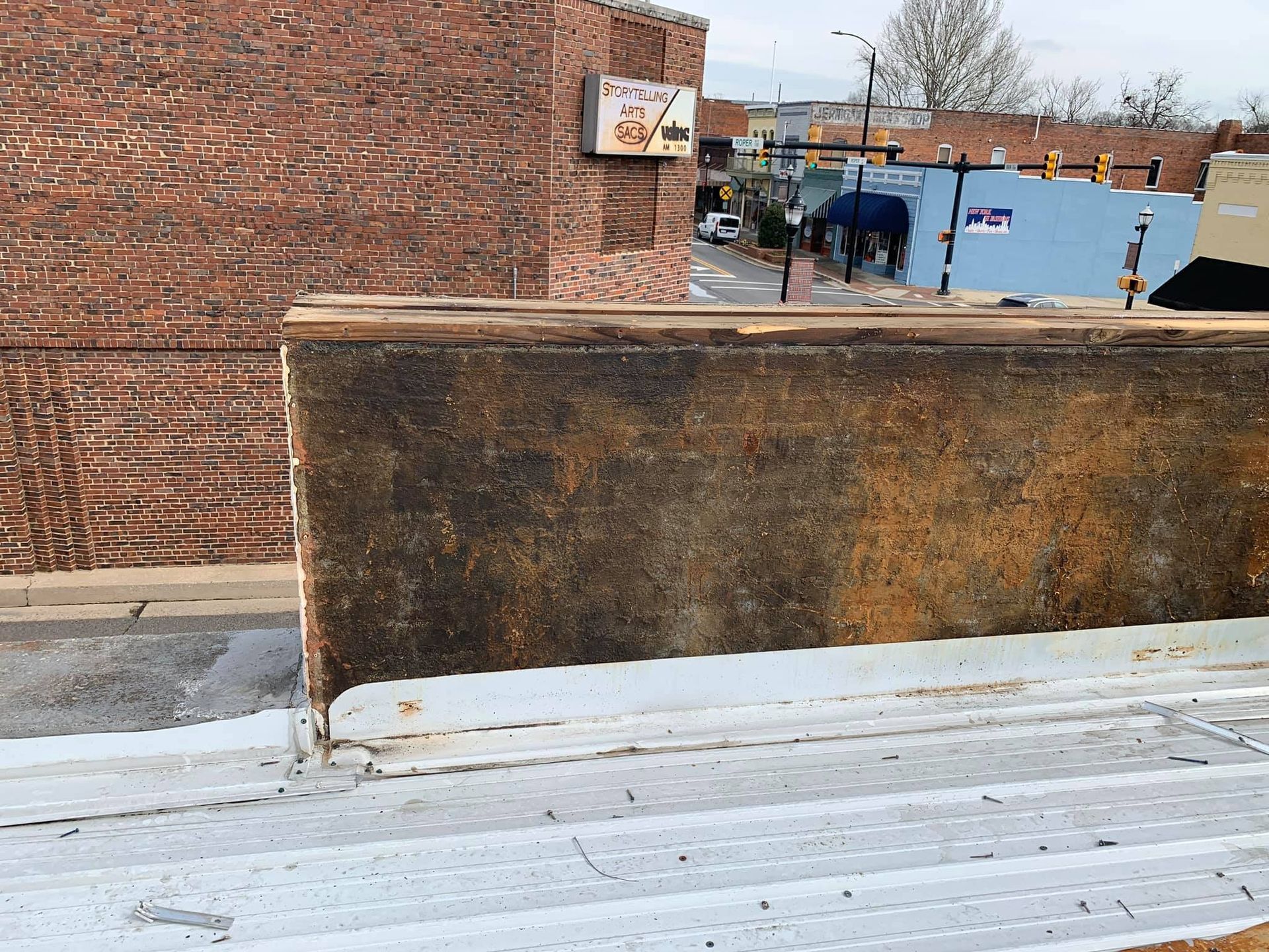 View of a building rooftop and street below; weathered brick, brown walls, and white metal accents.