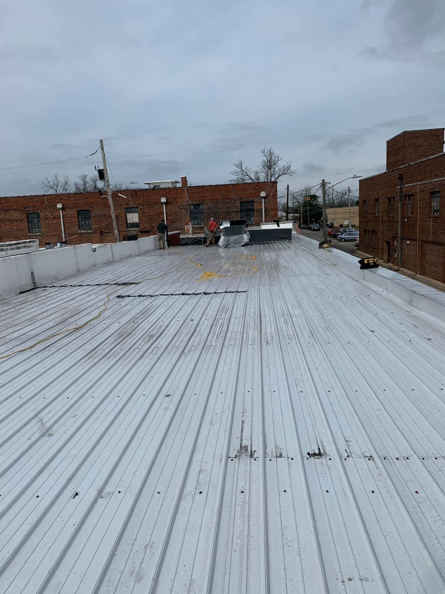 White corrugated metal roof with red brick buildings in background under overcast sky.