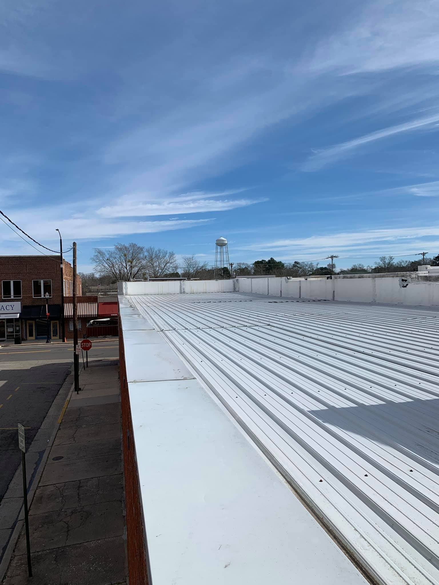 View from a building roof looking down on a street. Buildings and water tower visible under blue sky.