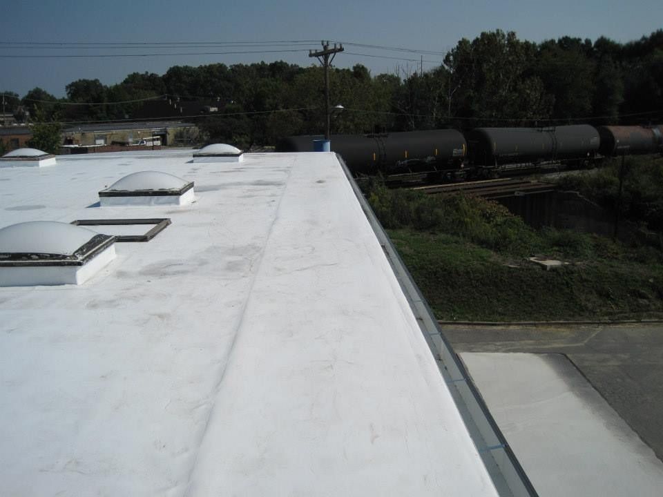 White commercial roof with skylights and edge, train cars in background.
