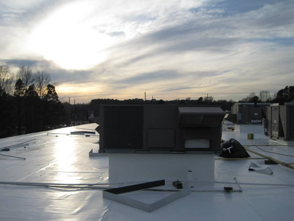 White commercial roof with HVAC units under a cloudy sunset.