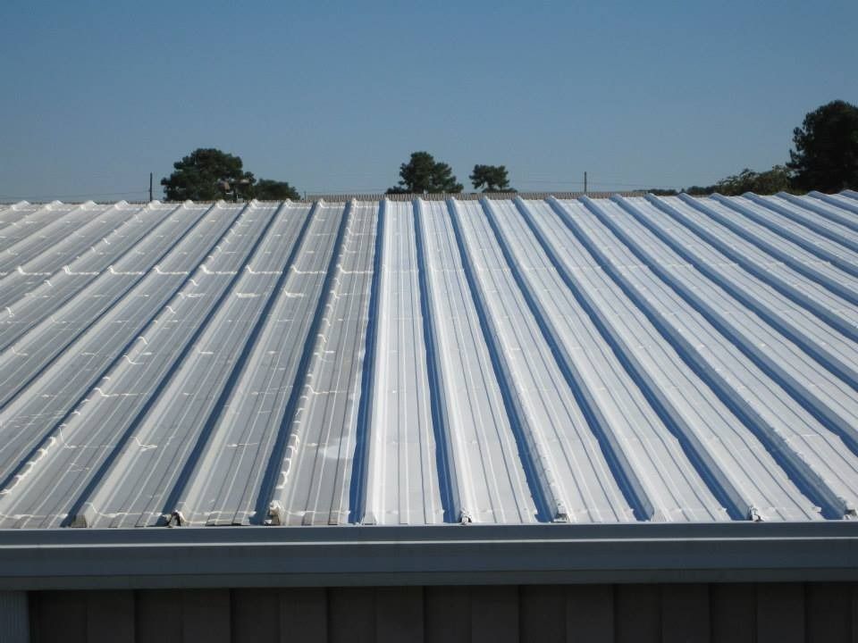 Metal roof with parallel ridges, reflecting sunlight on a clear day.