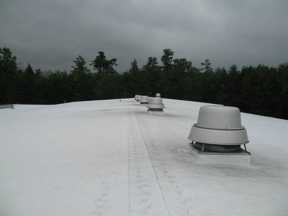 White commercial roof with vents under a cloudy sky, trees in the background.