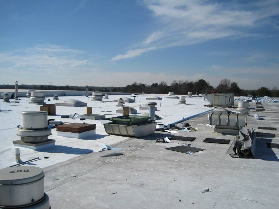 White commercial rooftop with vents and mechanical equipment under a blue sky.