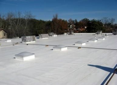 White commercial roof with skylights and HVAC units on a sunny day.