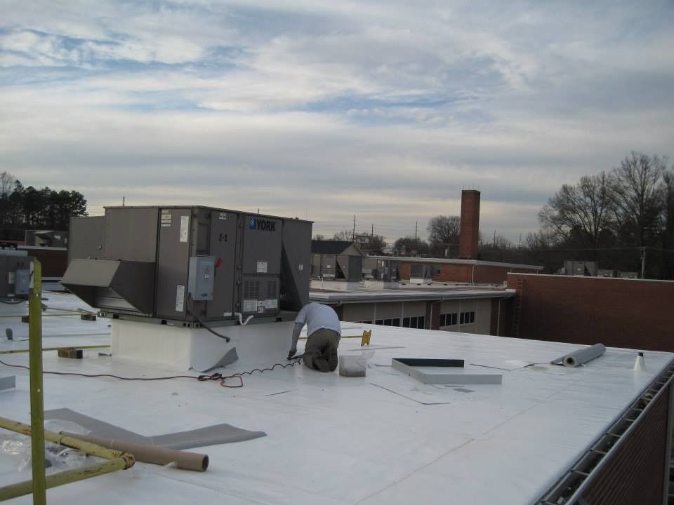 Rooftop with HVAC units and a person working on a white roof, under cloudy skies.