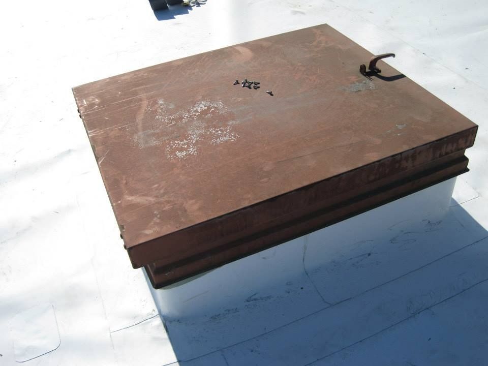 Rusty metal roof access hatch on white roofing.