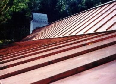 Copper metal roof with raised seams and a chimney in the background.