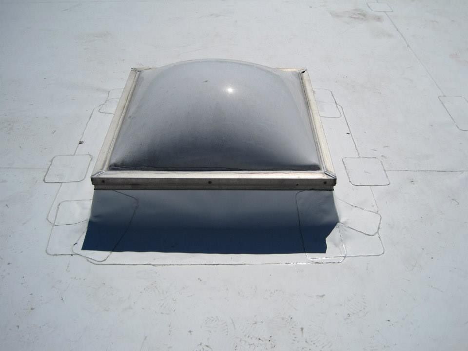 Skylight on a white flat roof. A dark dome is in a silver frame.