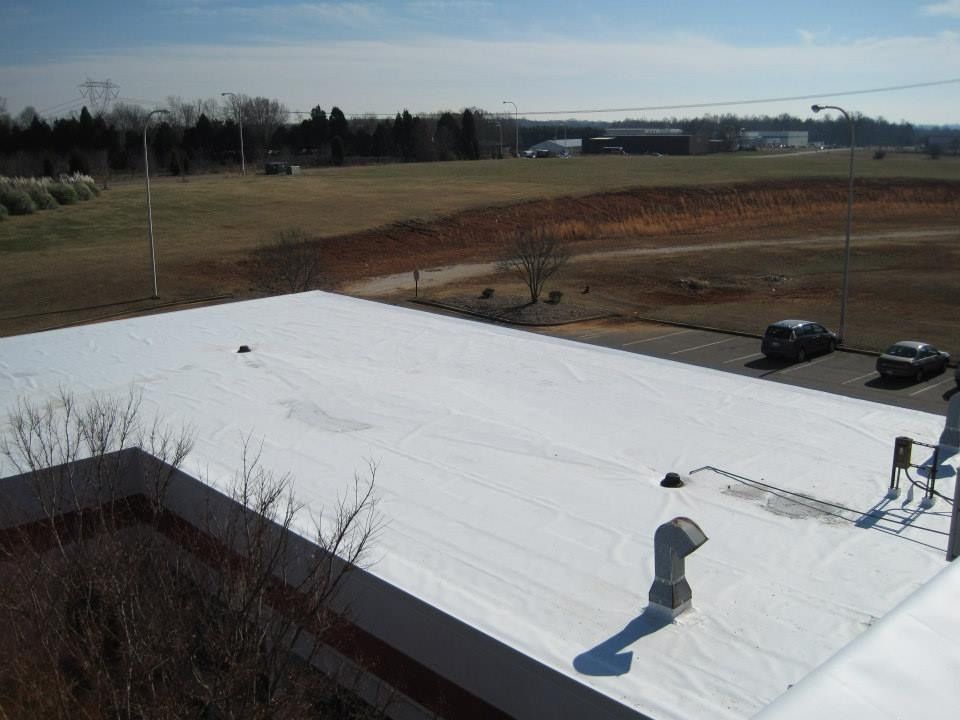 White rooftop with landscape view, trees, and parked cars under a blue sky.