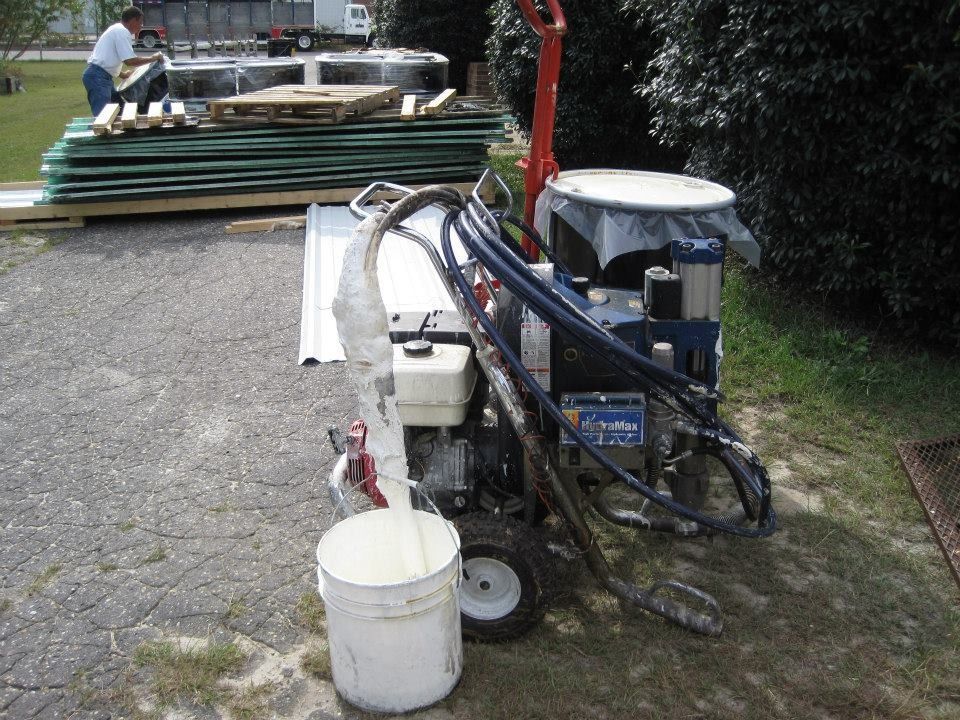 Paint sprayer with a white bucket, a person nearby, and construction materials.