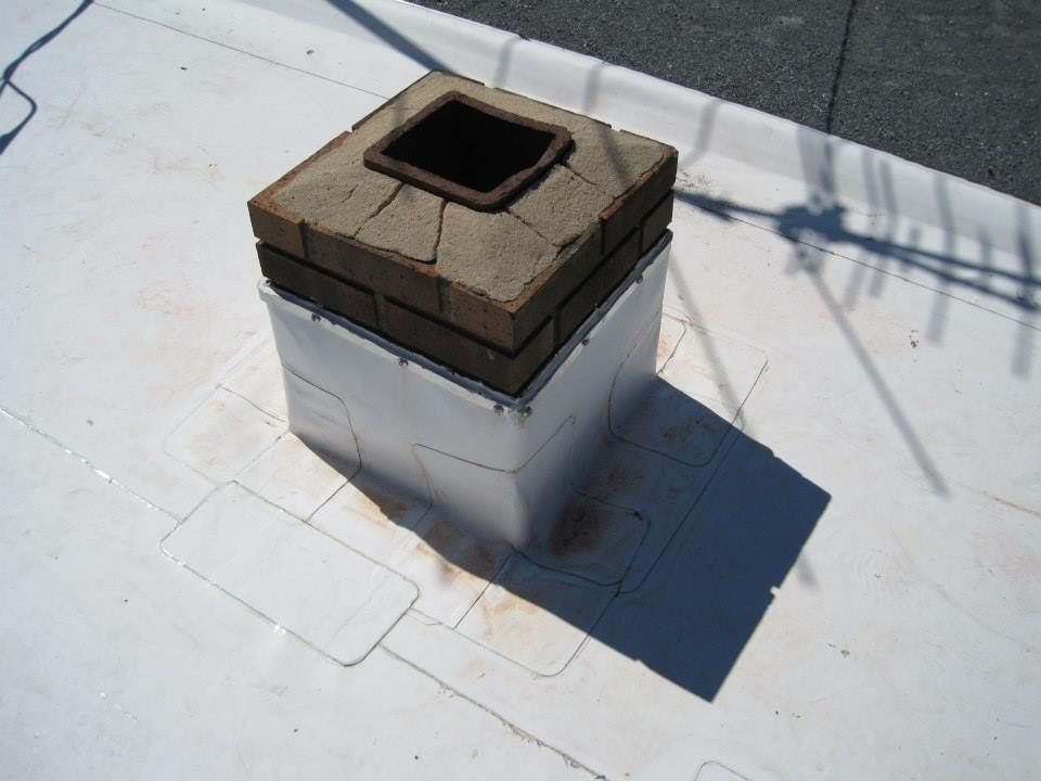 Chimney on a white flat roof, showing cracked brick and white flashing.