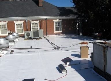White flat roof with vents and air conditioning units near a brick building.