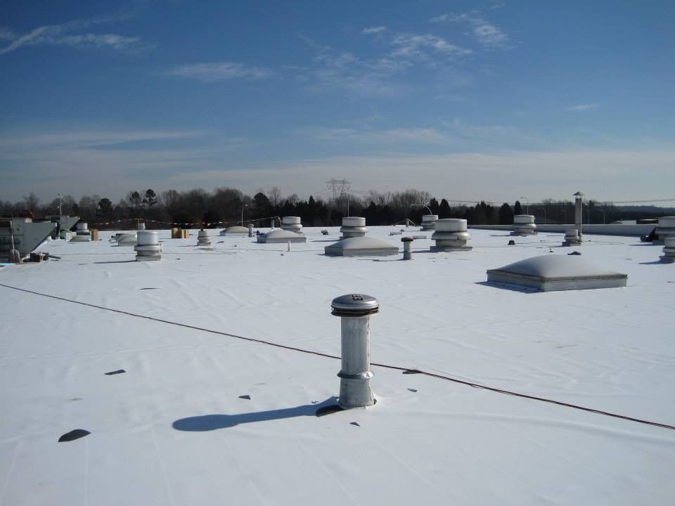 Snow-covered flat rooftop with various vents and skylights under a blue sky.