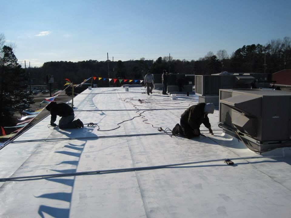 Roofers working on a flat roof, installing or repairing roofing material under a bright sky.