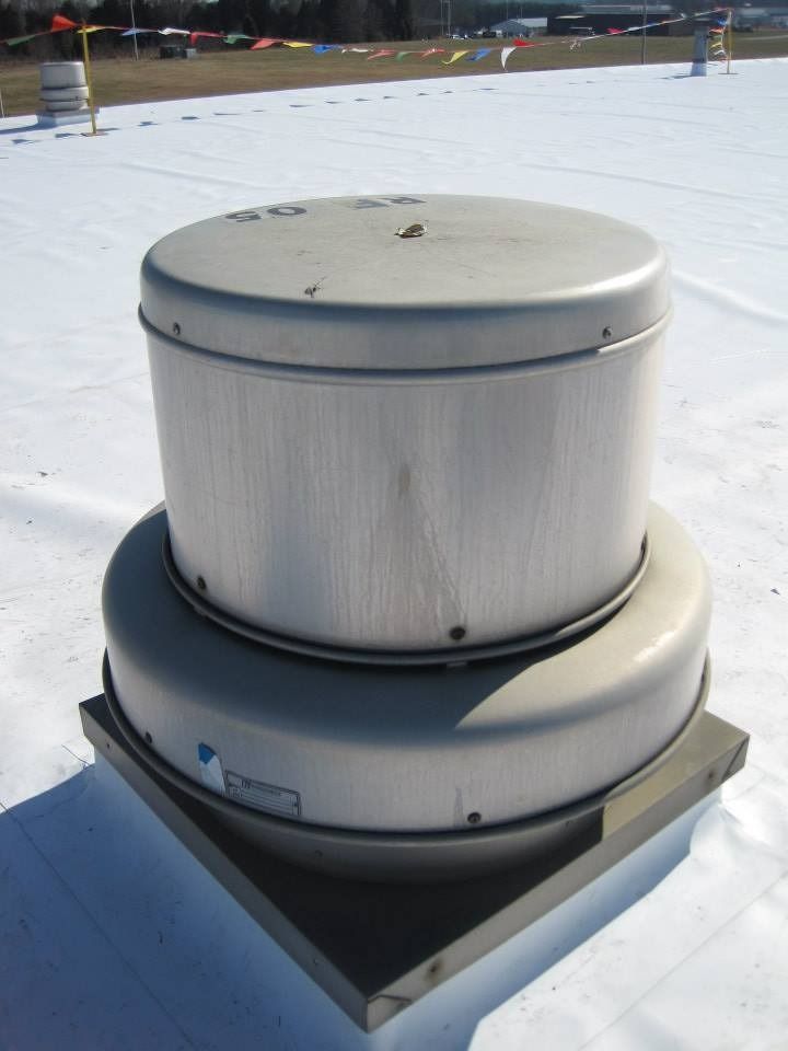 Gray cylindrical roof exhaust fan on a white roof, outdoors on a sunny day.
