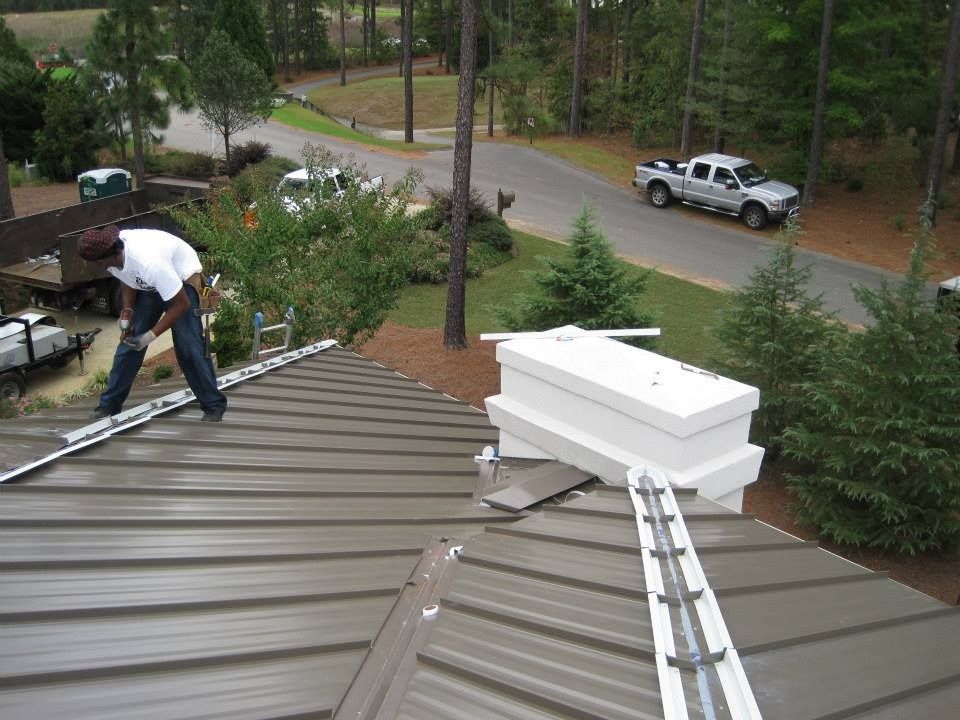 Roofer installing metal roofing on a house, tools and materials visible. Exterior view of a residential property.