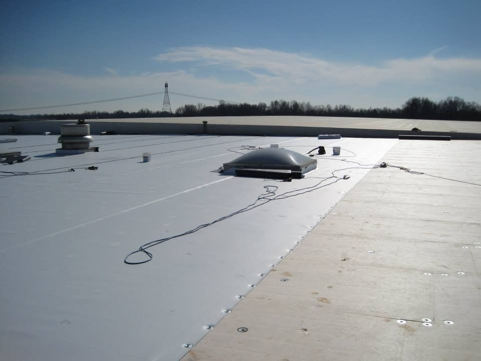 Flat white commercial roof with a skylight, power lines, and a distant treeline under a blue sky.