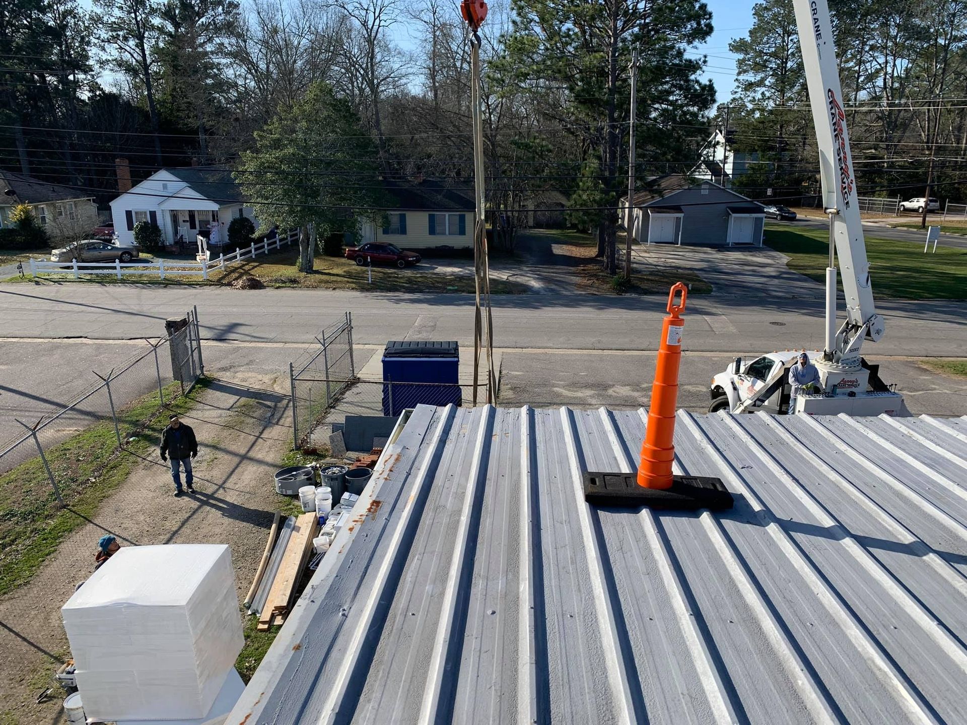 Person walking near a metal roof with an orange safety cone. Buildings and a crane are in the background.