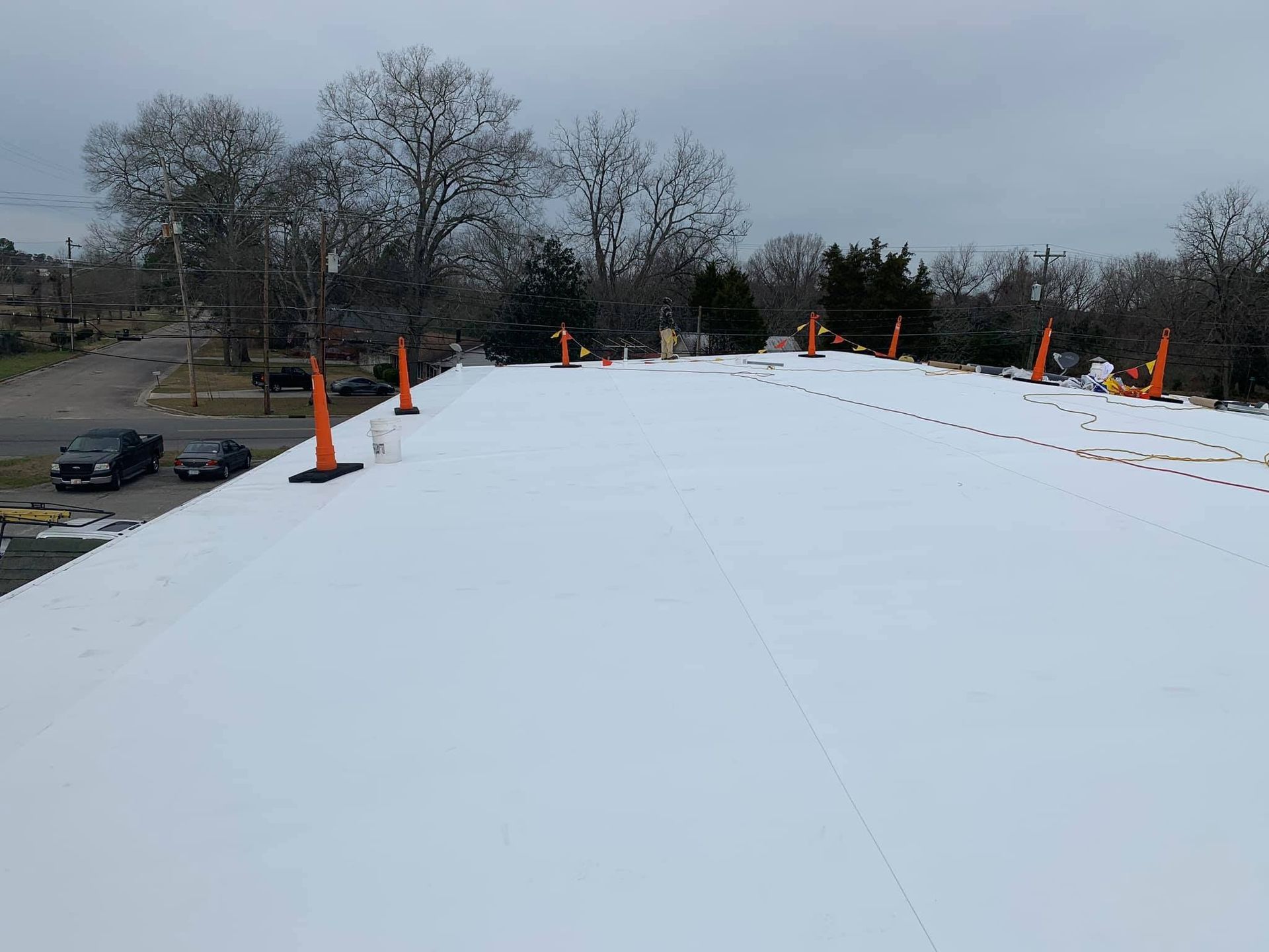White flat roof with orange cones; trees and vehicles in the distance on an overcast day.