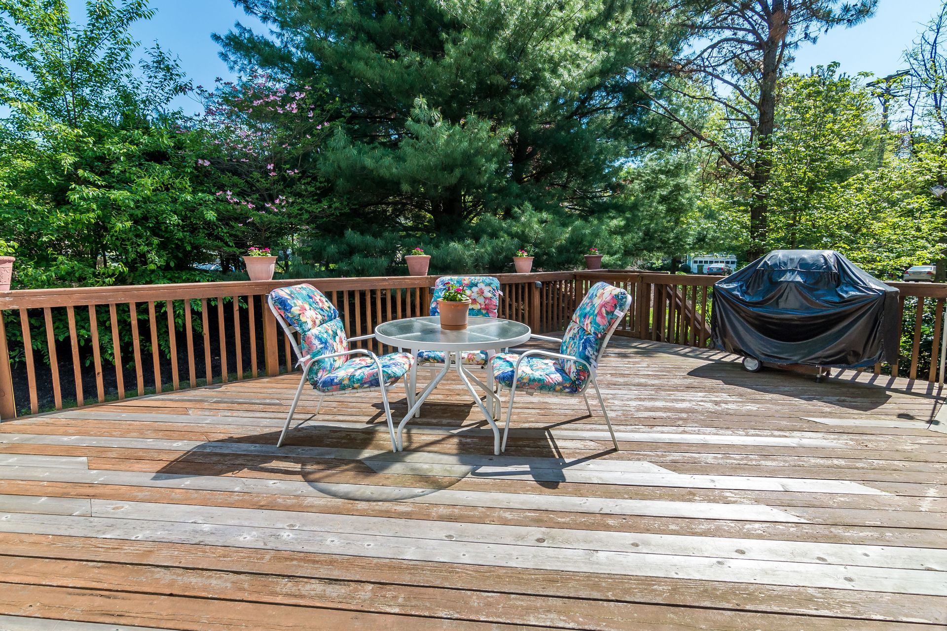 Wooden deck with table and chairs; barbecue grill in the corner; trees in the background.