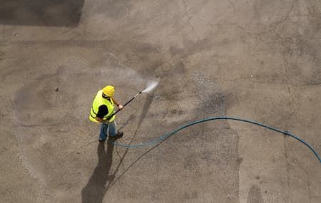 Person in yellow vest power washing concrete.