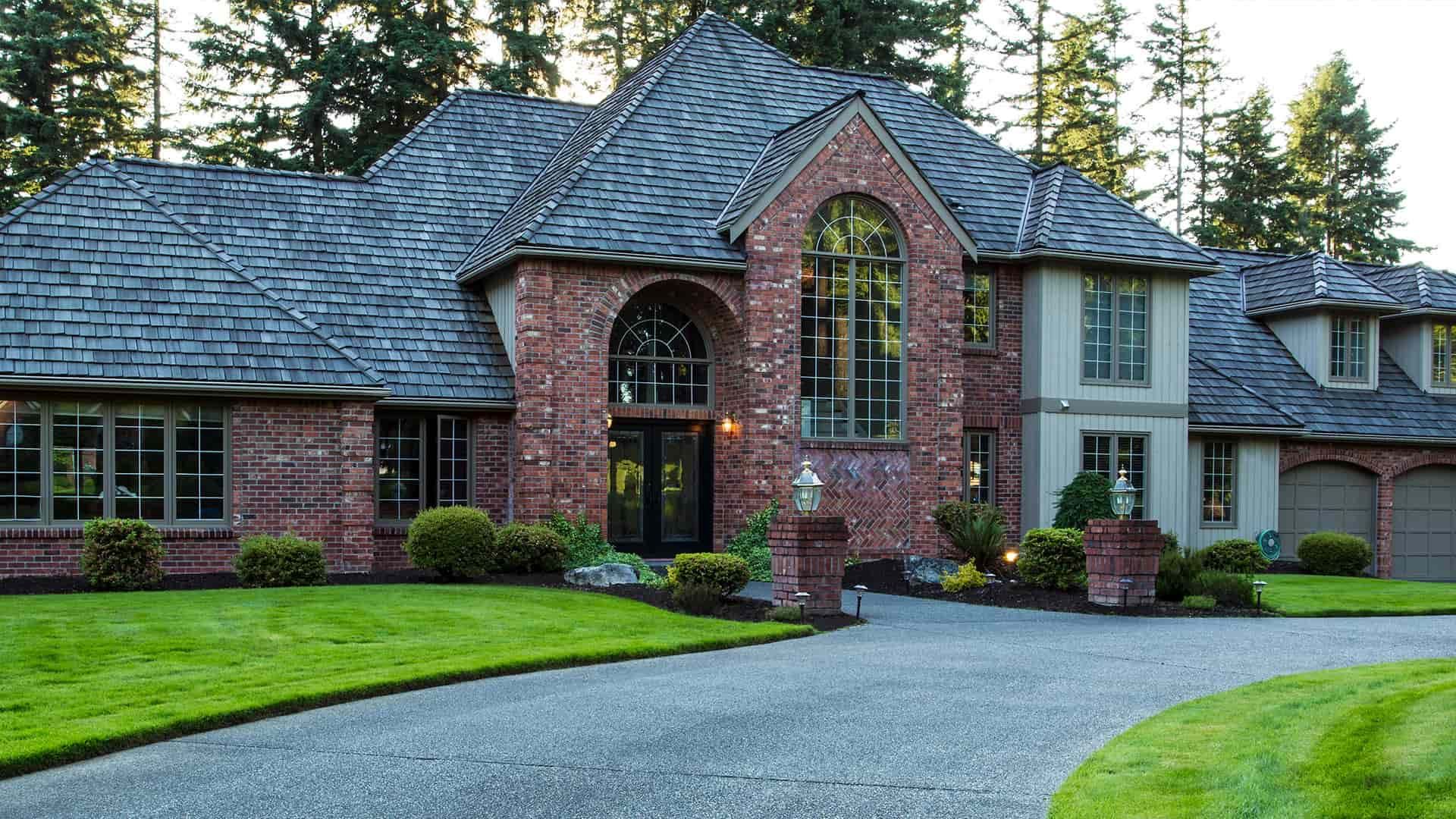 Two-story brick and stone home with gray roof, arched entrance, and green lawn.