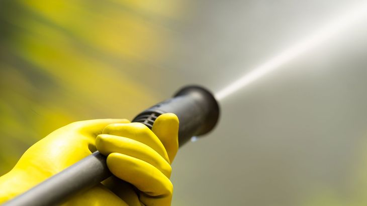 Hand in yellow glove holds pressure washer, spraying water.