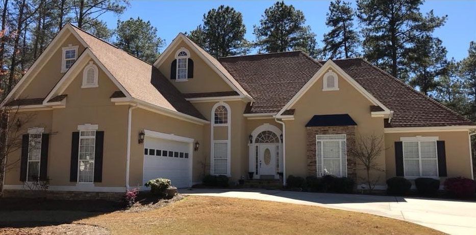 Beige two-story house with dark roof and shutters, white garage door and front door, on a sunny day.