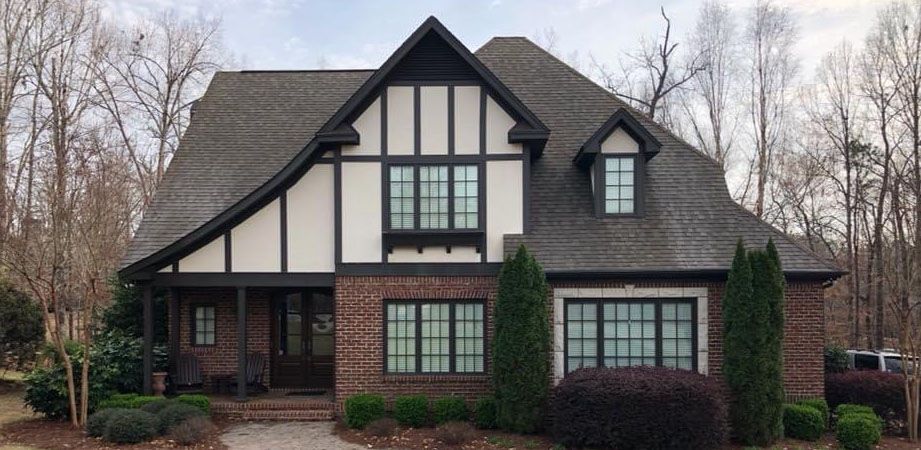 Tudor-style brick house with dark trim, a gray roof, and green shrubbery.