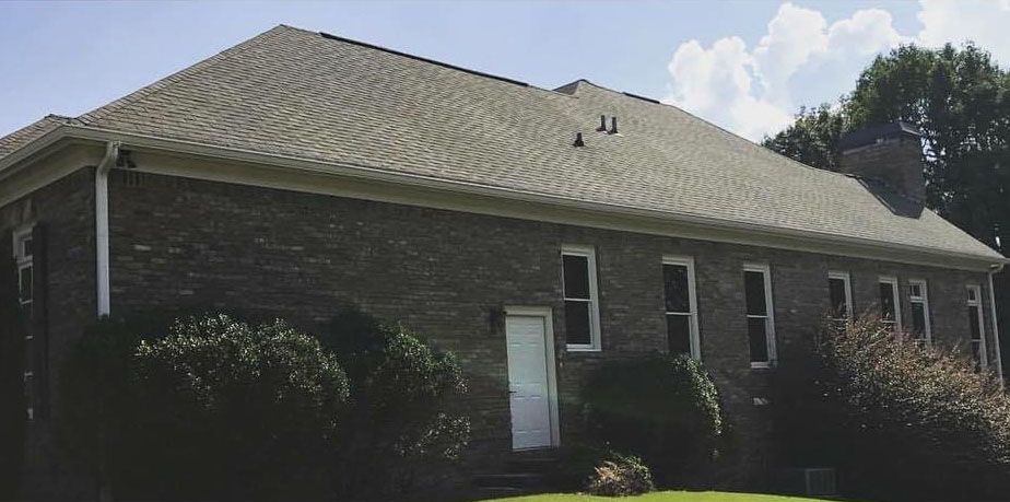 Brick building with windows, a white door, and a gray roof under a blue sky.
