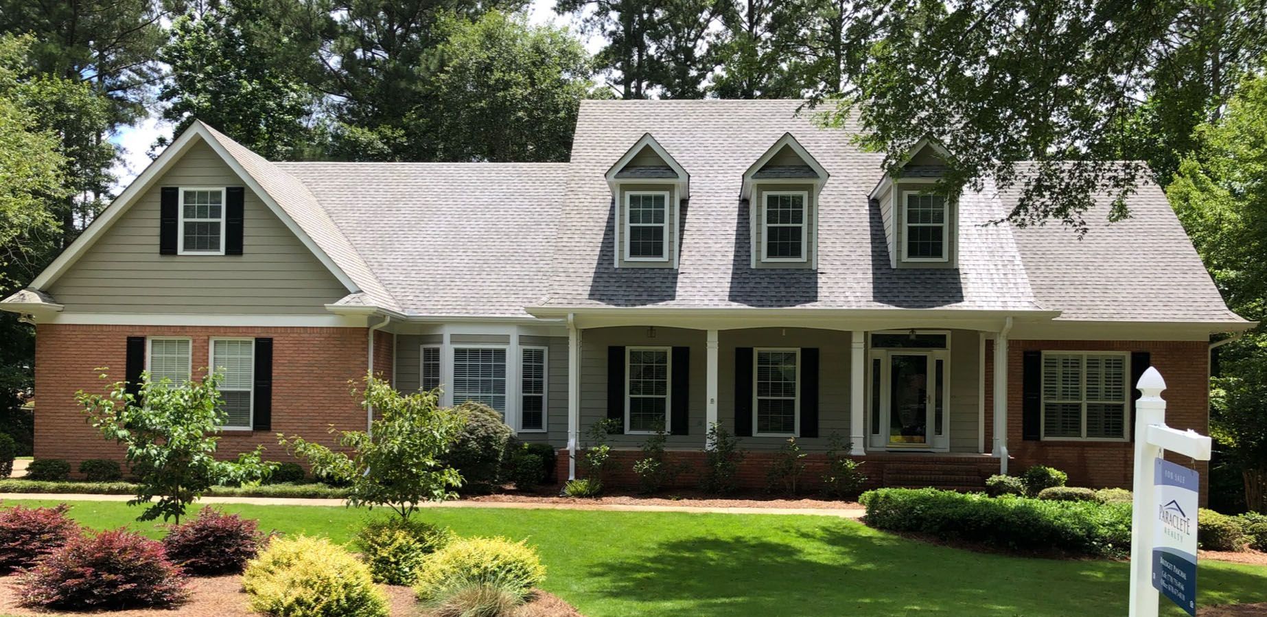 A two-story brick house with a green lawn and trees, sunny day.