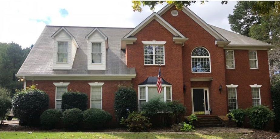 Red brick house with grey roof, American flag, and bushes.