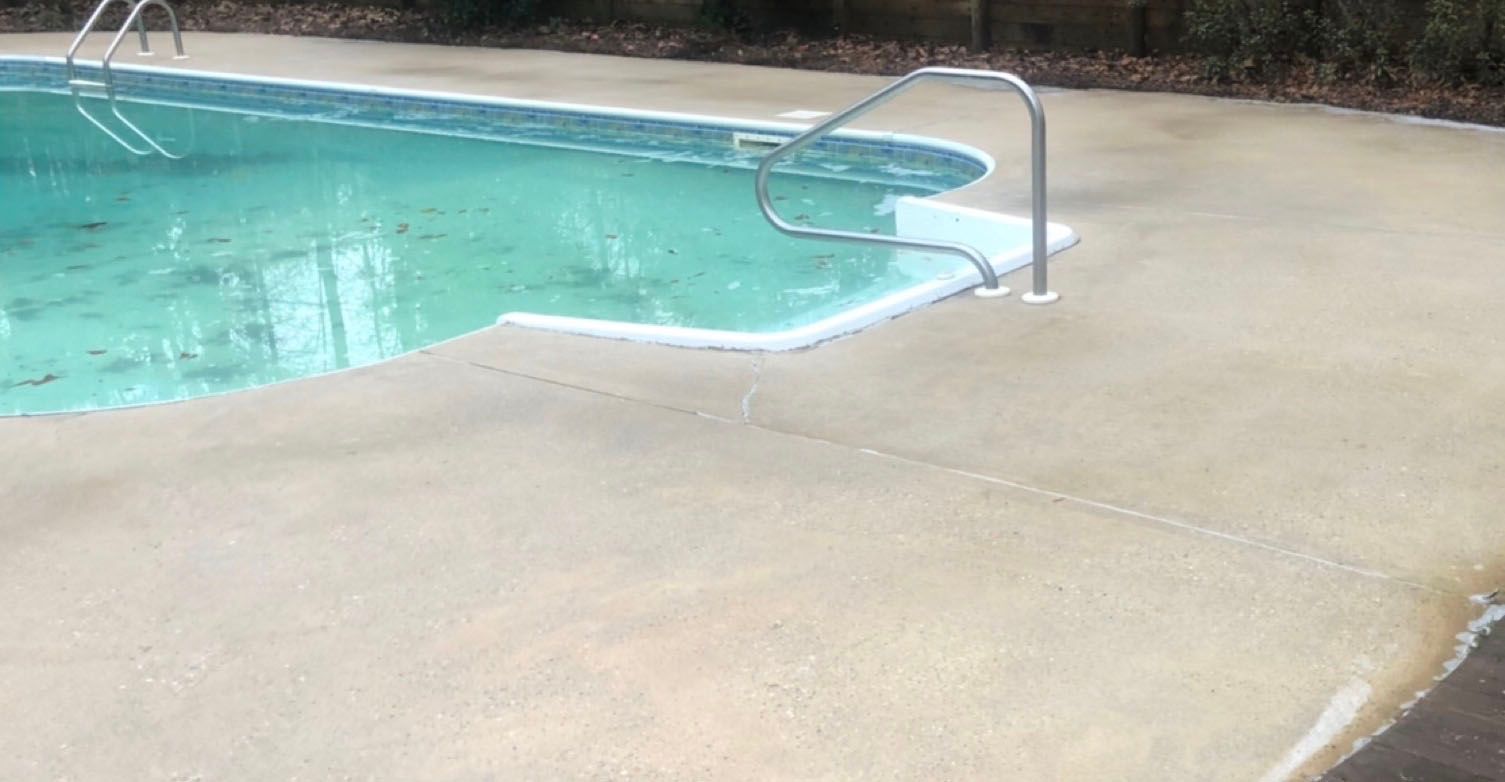 Pool with concrete surround, handrails, and turquoise water; trees in the background.