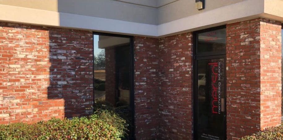 Brick building entrance with large windows and a red door. Red lettering is visible on the door.