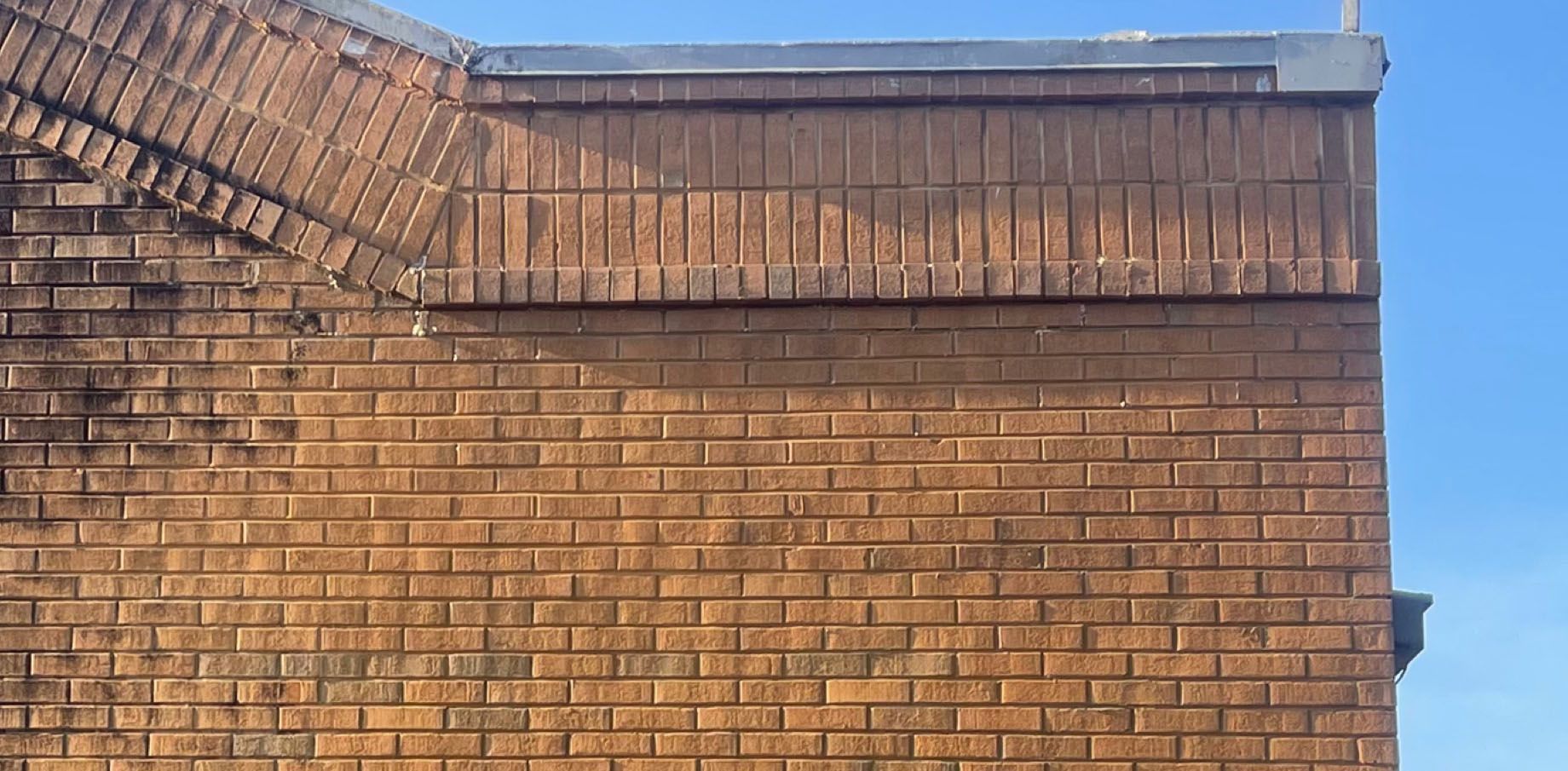 Brick building exterior with arched detail and clear blue sky.
