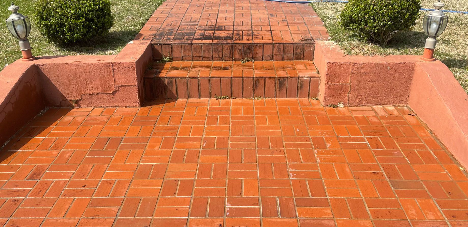 Brick walkway leading to steps, flanked by bushes and topped with lights.