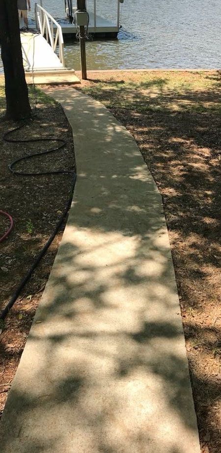 Concrete path leading to a dock on a lake, with shadows of trees on the path.