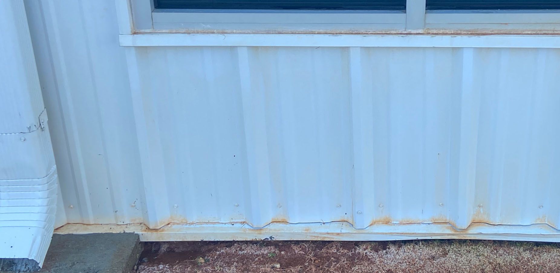 White corrugated metal siding with a window and some rust near the base.