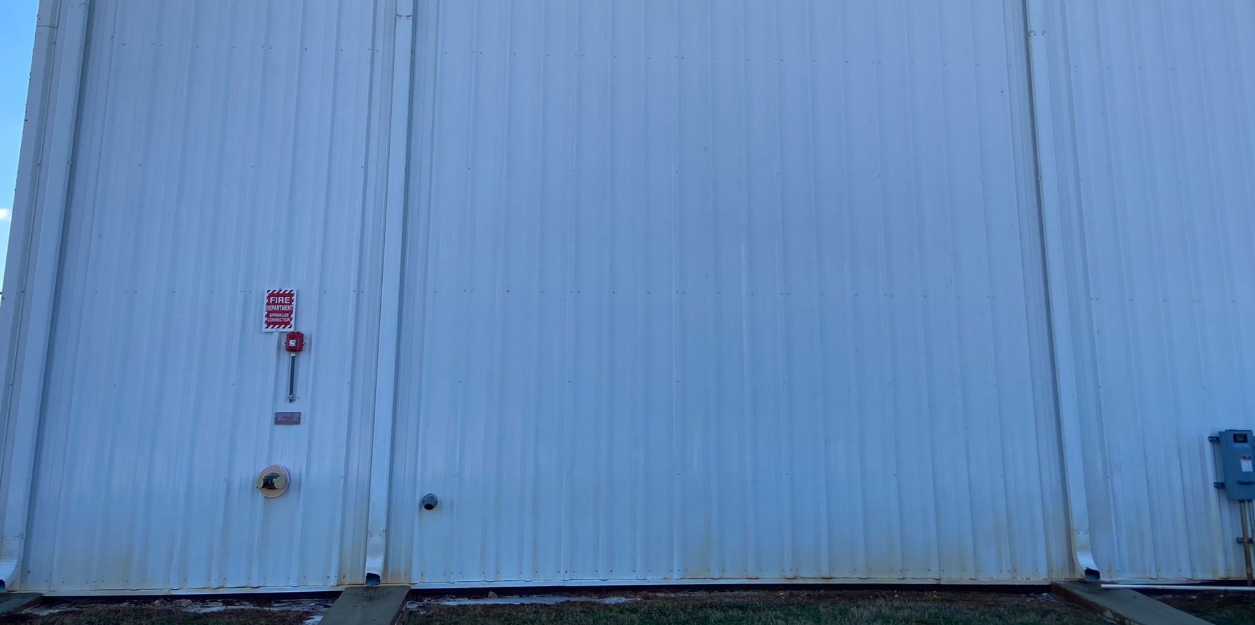 A white metal building with a fire alarm system on the left side, with a blue sky in the background.
