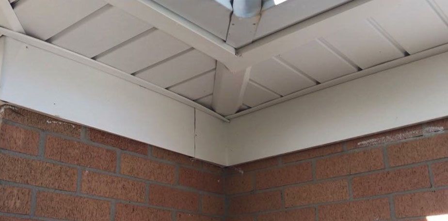 Corner of a building with a white roof, brick wall and a downspout.
