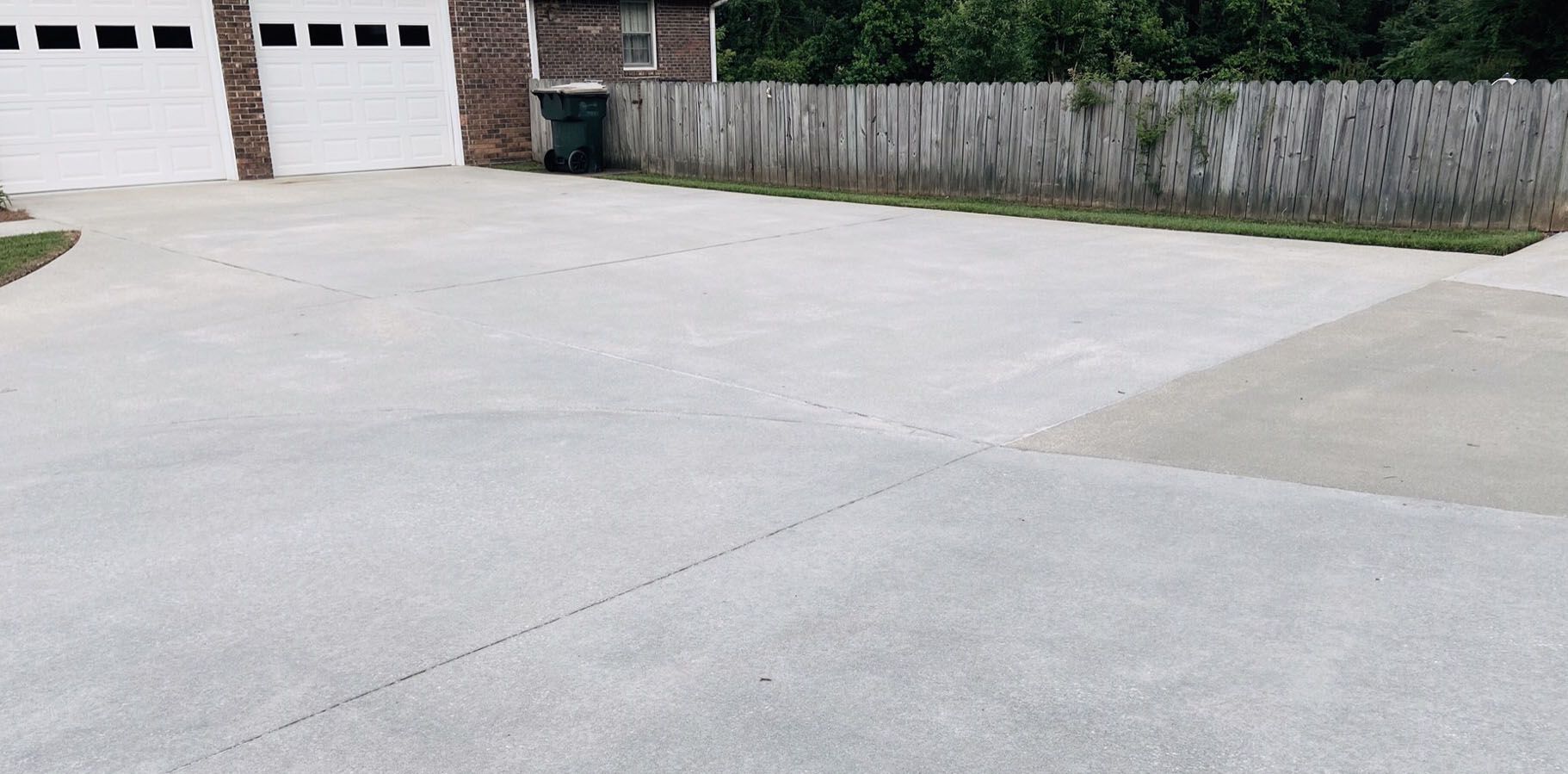 Concrete driveway leading to a house with a garage and a wooden fence.