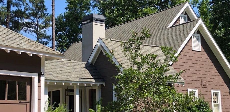 House with brown siding and grey roof, set against a backdrop of trees.